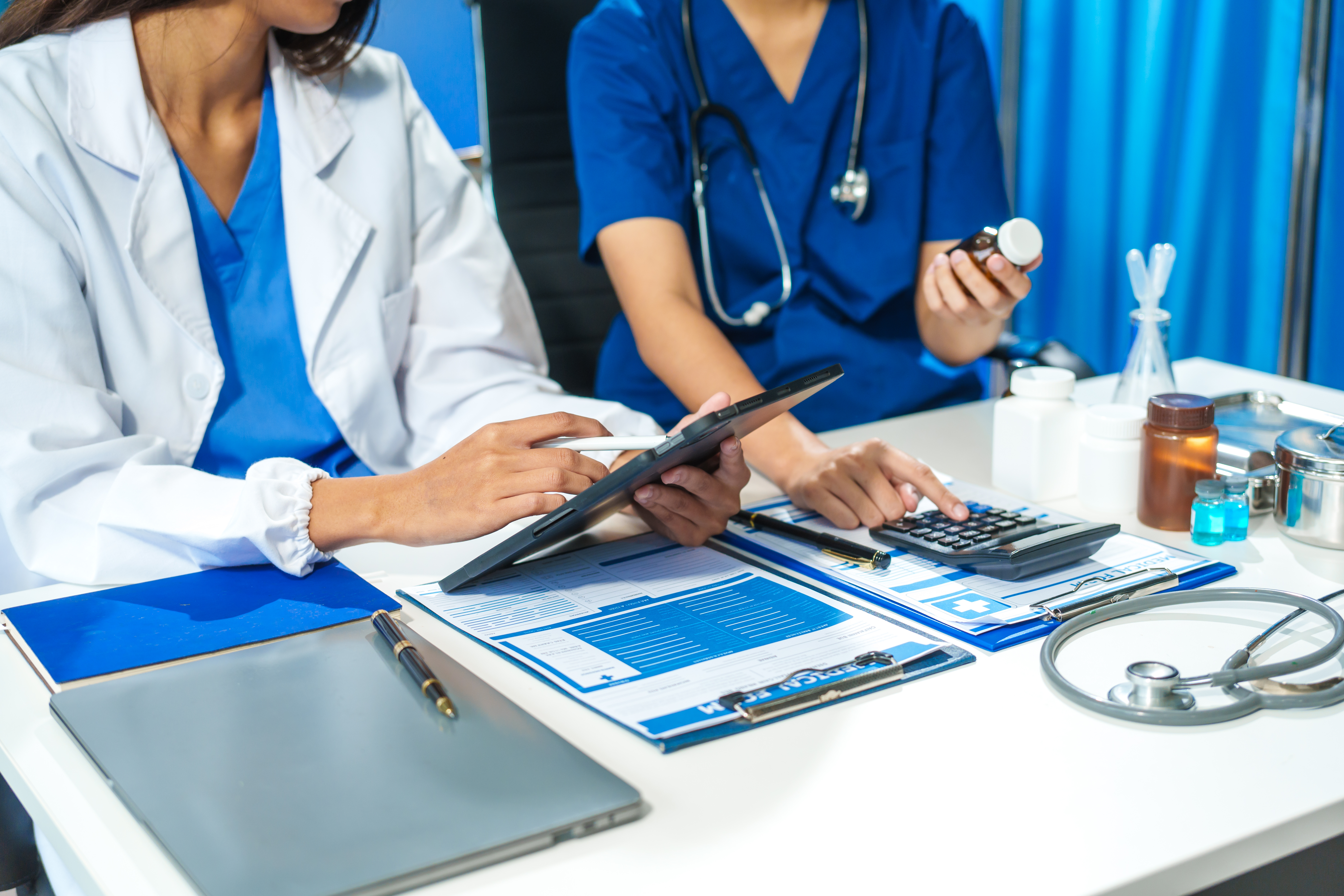 A close-up of two doctors discussing a bottle of medicine at a table in a hospital. They collaborate on patient treatment, analyzing medicine, planning care, and using advanced technology