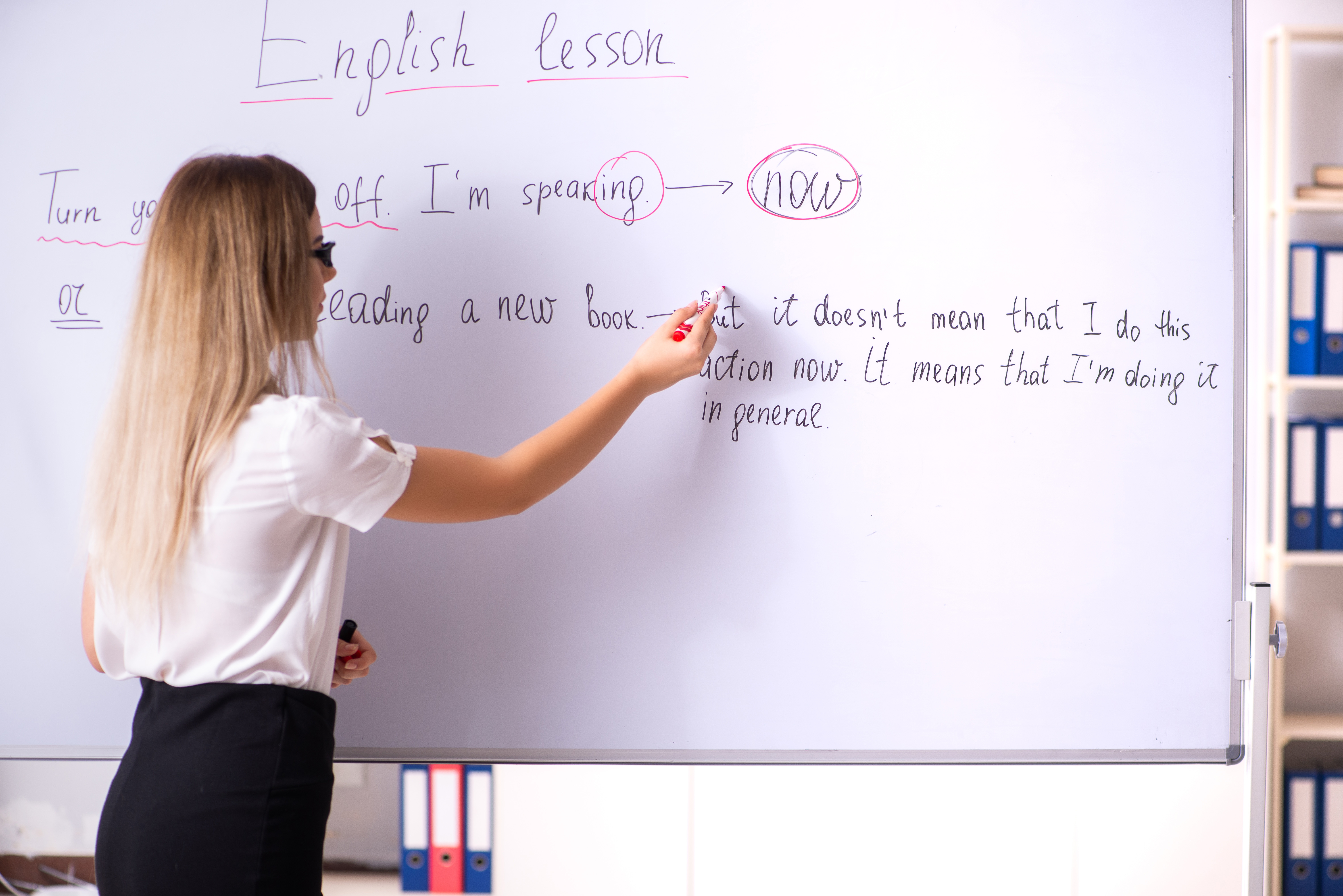 Young female english language teacher standing in front of the blackboard   