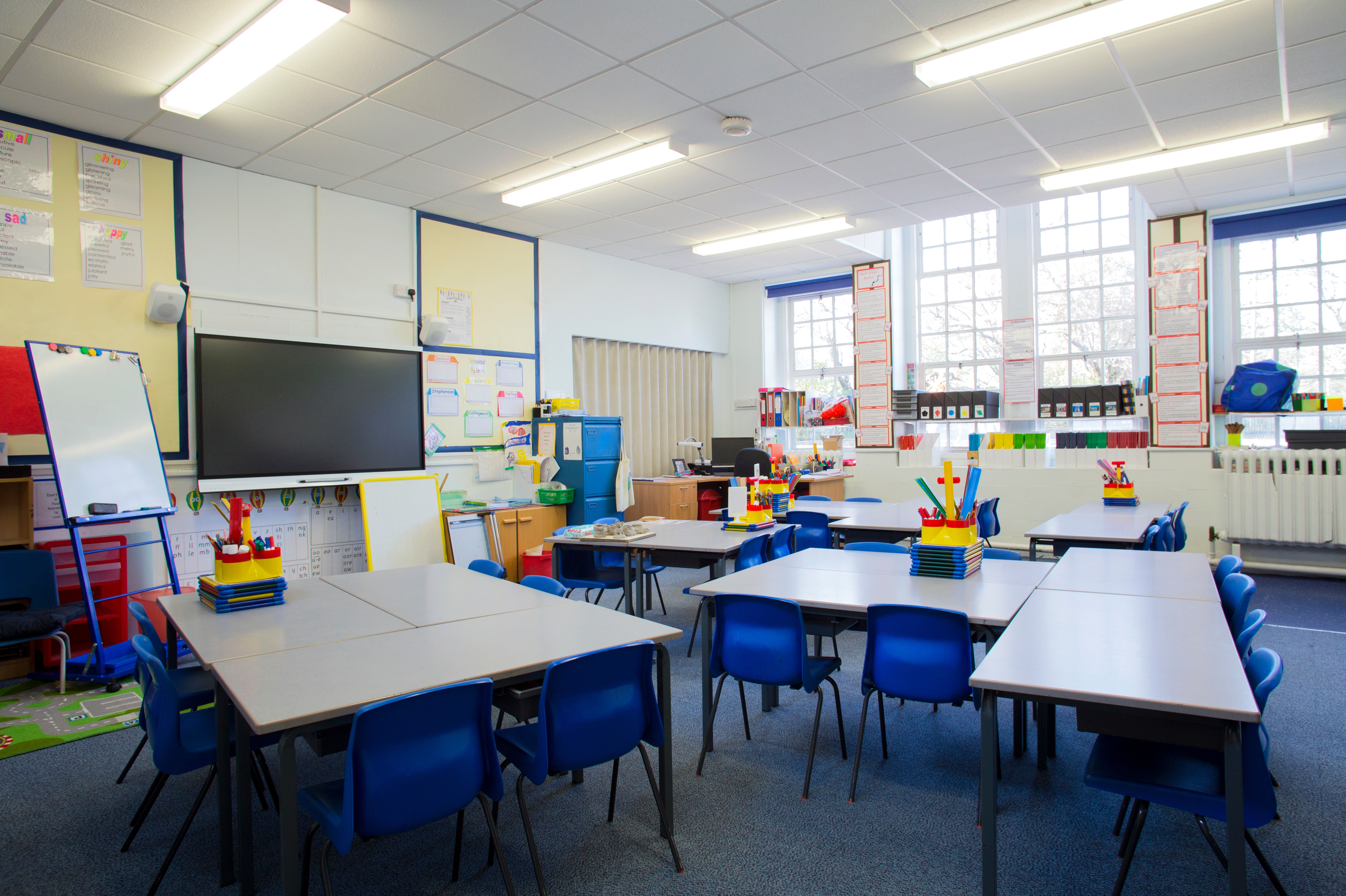 A horizontal image of an empty primary school classroom. The setting is typically British.