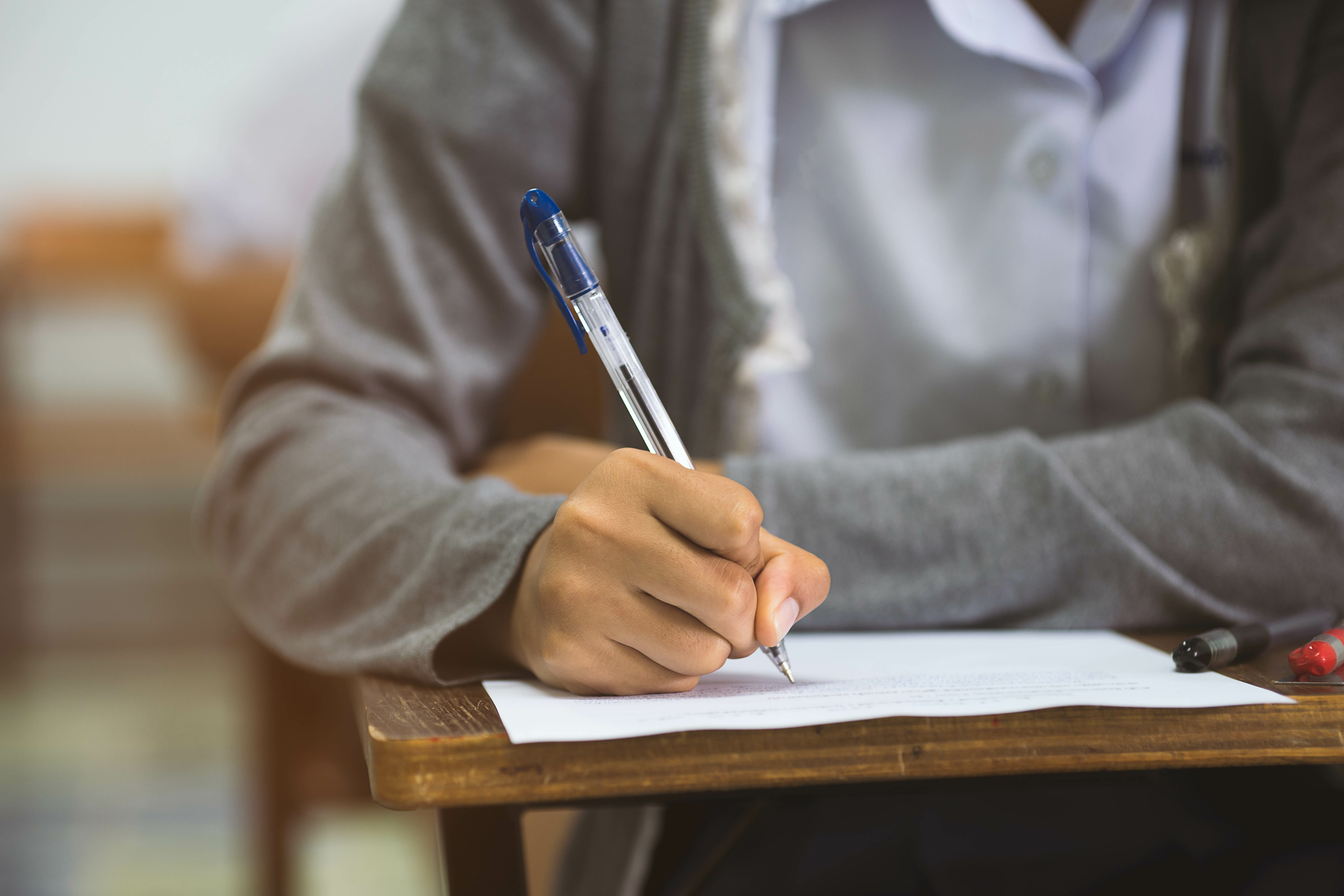 Close up hand of student reading and writing exam with stress in classroom.