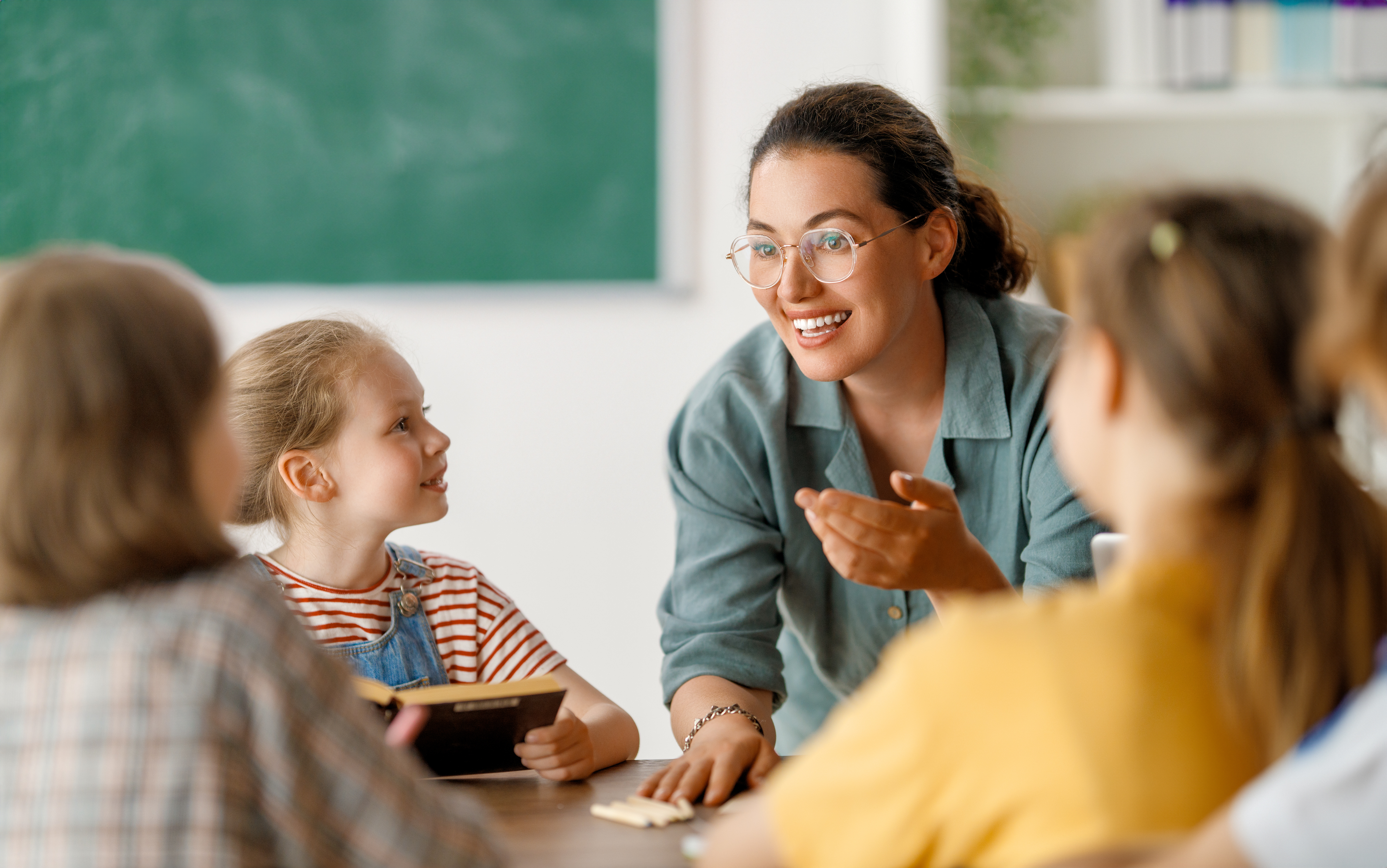 Happy kids and teacher at school. Woman and children are talking in the class.