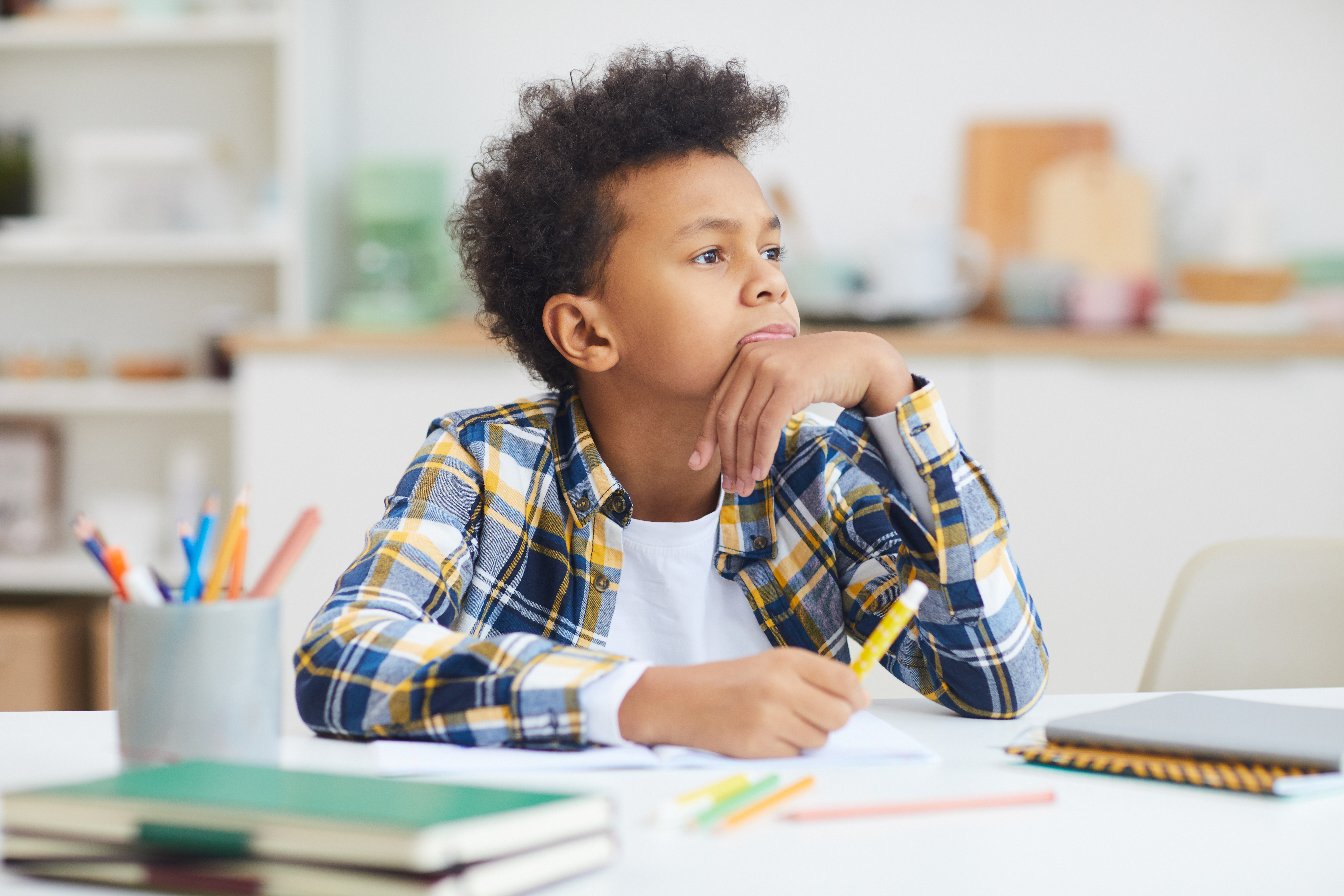Portrait of teenage African-American boy daydreaming at desk while doing homework, copy space