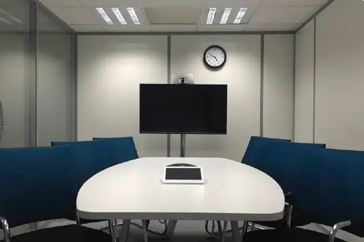 Compact huddle room with curved bench seating, a round table, and a wall-mounted display.