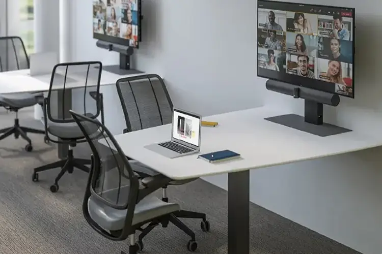 Custom office furniture arrangement with dual monitors, a laptop, and meeting chairs.